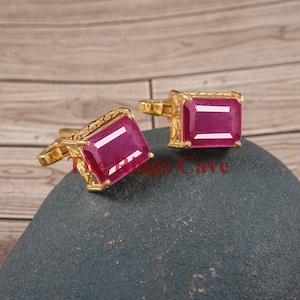 Puede incluir: Un par de gemelos de oro, cada uno con una piedra preciosa roja. Las piedras preciosas son de talla esmeralda y tienen un alto pulido.