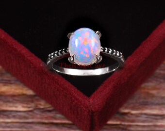 Puede incluir: Un anillo de plata con una gran piedra de ópalo ovalada engastada en una montura de garras. La banda está decorada con pequeñas piedras negras.