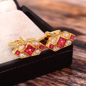 May include: Gold cufflinks featuring a red ruby and white diamonds set in a geometric design.