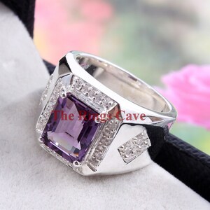 Könnte beinhalten: Ein silberner Ring mit einem großen, rechteckigen, violetten Amethyst-Edelstein, der von kleineren, klaren Edelsteinen umgeben ist. Der Ring hat ein quadratisches Design und ist in eine silberne Band gefasst.