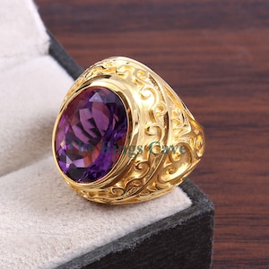 May include: A gold ring with an ornate design and a large oval amethyst gemstone.