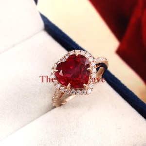 Pode incluir: Um anel de noivado de rubi em forma de coração com um halo de diamantes menores engastados em ouro rosa.