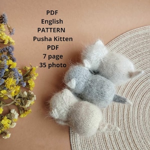 Puede incluir: Tres juguetes de gatito de punto gris y blanco sobre una superficie beige. El texto "PDF English PATTERN Pusha Kitten PDF 7 page 35 photo" es visible en la imagen.