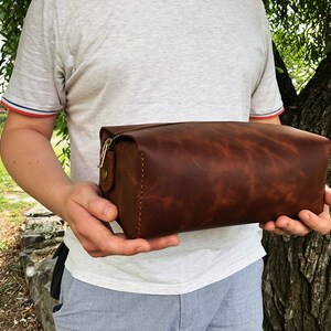 May include: A brown leather toiletry bag with a zipper closure and gold hardware.