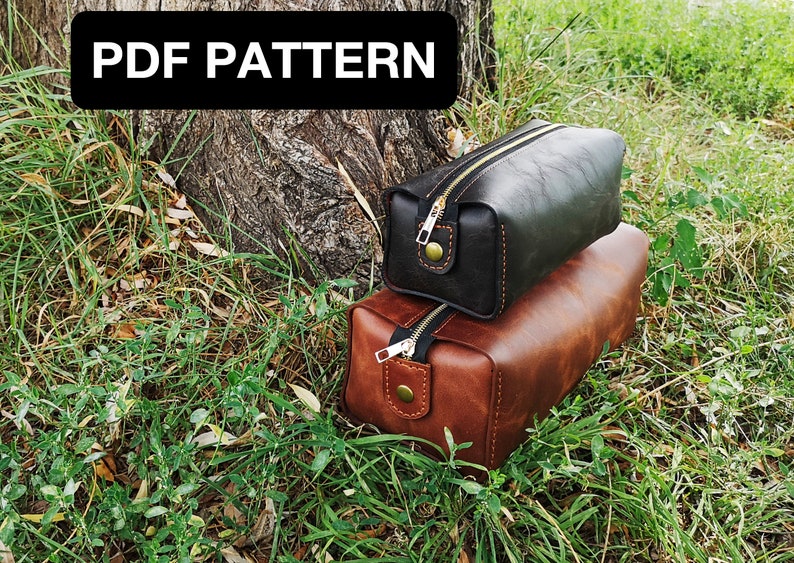 May include: Two leather zippered pouches, one brown and one black, are stacked on top of each other. The pouches are sitting on a bed of green grass. The text "PDF PATTERN" is visible at the top of the image.