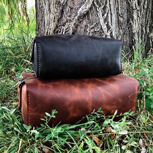 May include: Two leather travel bags stacked on top of each other. The top bag is black and the bottom bag is brown.