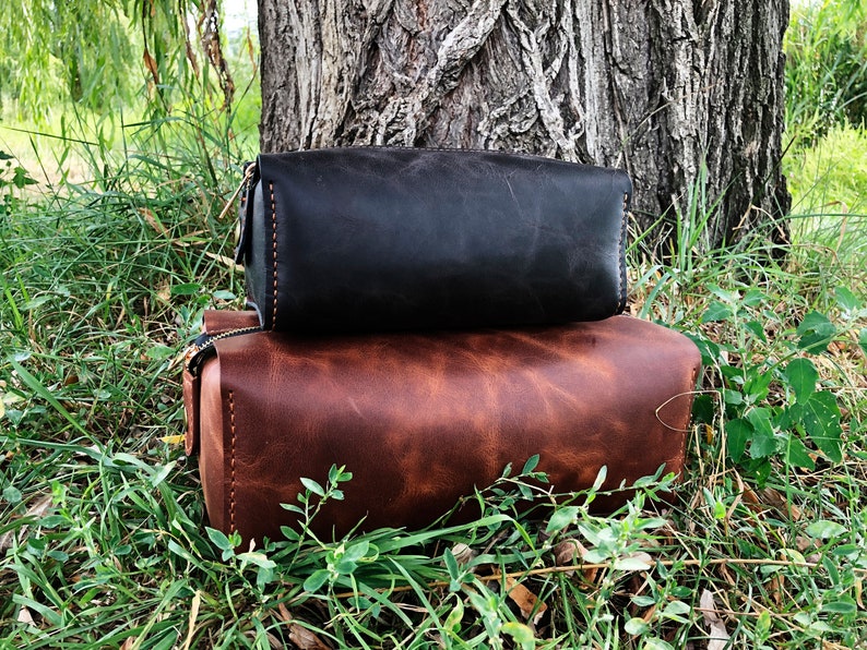 May include: Two leather travel bags stacked on top of each other. The top bag is black and the bottom bag is brown.