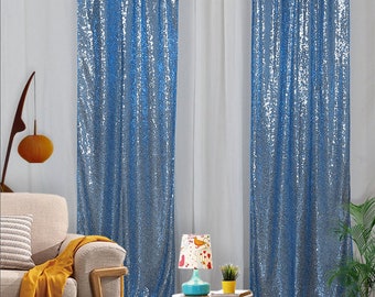 May include: Two blue sequin curtains hanging in a room with a sofa, a lamp, and a plant. The curtains are made of a shimmering fabric with a subtle iridescent sheen.