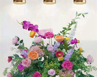 May include: A vibrant floral arrangement featuring a variety of colorful flowers, including roses, orchids, and other blooms. The arrangement is set against a neutral background with three gold pendant lights.