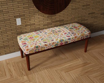 May include: A rectangular bench with a floral patterned cushion in shades of yellow, blue, pink, and green. The bench has a dark brown wooden frame and four tapered legs. The bench is a decorative furniture piece.