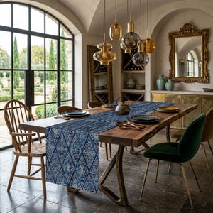 May include: A dining room table set with a blue and white patterned table runner. The table is made of wood and has metal legs. There are plates, utensils, and a teapot on the table. The room has a large window and decorative lighting.