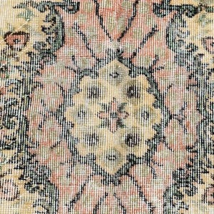 May include: Close-up of a vintage rug with a detailed floral pattern. The rug features a cream-colored background with a central medallion design in shades of pink, green, and black. The intricate design is typical of traditional rug making.