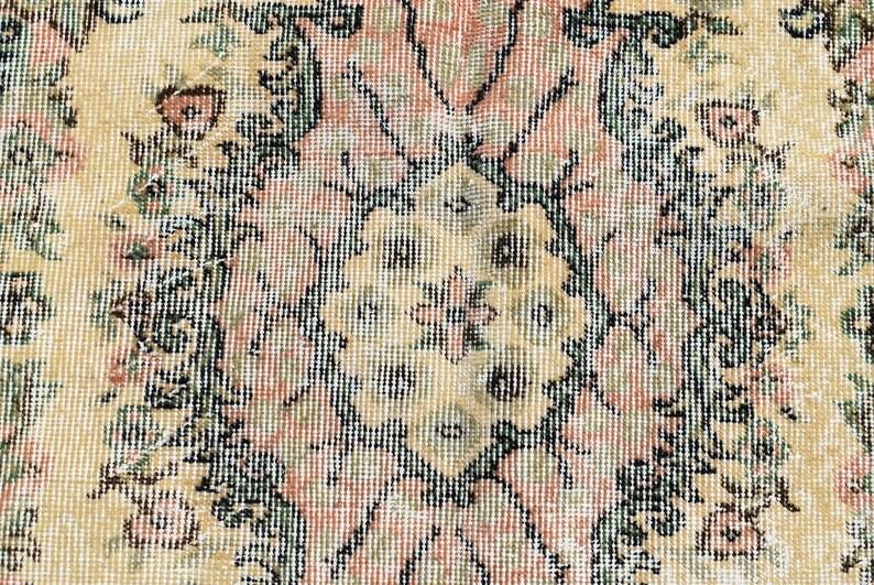 May include: Close-up of a vintage rug with a detailed floral pattern. The rug features a cream-colored background with a central medallion design in shades of pink, green, and black. The intricate design is typical of traditional rug making.