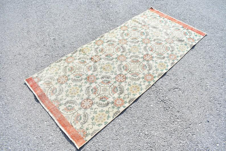 May include: Rectangular rug with a floral pattern in cream, orange, and green. The rug has a distressed look with an orange border. The design features repeating floral medallions and other floral elements. This rug is suitable for home decor.
