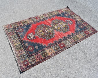 May include: A vintage red, blue, and yellow patterned rug with a geometric design. The rug has a fringed edge and is made of wool.