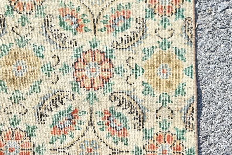 May include: Close-up of a beige rug with an intricate floral pattern. The design features orange, red, and green flowers, with black decorative elements. The rug has a vintage, traditional style, suitable for home decor.