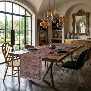 May include: A dining room scene featuring a large wooden table with a patterned runner. The table is set with plates, cutlery, and a teapot. Overhead, several pendant lights hang, and a large window offers a view of a garden.