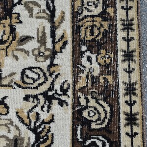 May include: Close-up of a brown and cream patterned rug with a geometric border. The rug has a traditional design with floral motifs.