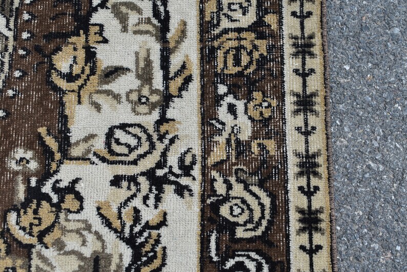 May include: Close-up of a brown and cream patterned rug with a geometric border. The rug has a traditional design with floral motifs.