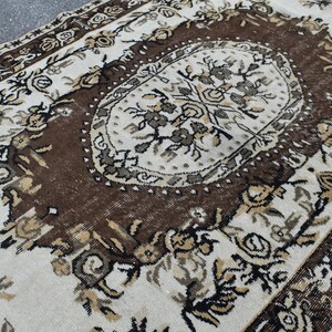May include: A vintage rug with a brown and white floral pattern. The rug has a central medallion with a geometric design.