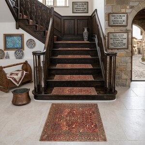 Peut inclure: Un escalier en bois sombre orné de tapis de marche rouges et bruns à motifs. Un grand tapis orné, avec un motif similaire, est posé au pied de l'escalier. Des panneaux en turc et en anglais sont visibles. L'ensemble crée une ambiance chaleureuse.