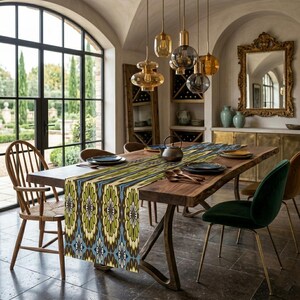 Pode incluir: Uma sala de jantar com uma mesa de madeira adornada com um caminho de mesa estampado em tons de azul, verde e amarelo. A mesa está posta com pratos e talheres. Várias lâmpadas pendentes estão penduradas por cima. Uma grande janela oferece vista para um jardim. A mesa tem cerca de 200 cm de comprimento.