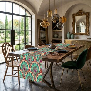 May include: A dining room table is set with a colorful table runner. The runner features a teal, red, and gold floral pattern. The table is made of wood and has metal legs. The room has large windows and decorative lighting.