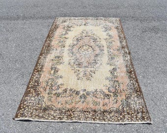May include: Rectangular vintage rug with a central medallion design in cream, peach, and brown tones. The rug features floral patterns and a dark brown border, adding a touch of classic elegance to any space.