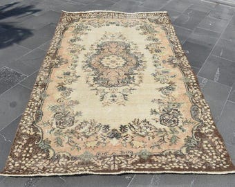 May include: An antique beige rug with a central floral medallion design and a detailed border. The rug features a faded, distressed look with accents of brown, peach, and green, suggesting a vintage or traditional style.