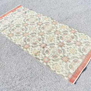 May include: Rectangular rug with a cream-colored background and a repeating floral pattern in shades of orange, green, and yellow. The rug has a faded, vintage look with an orange border.