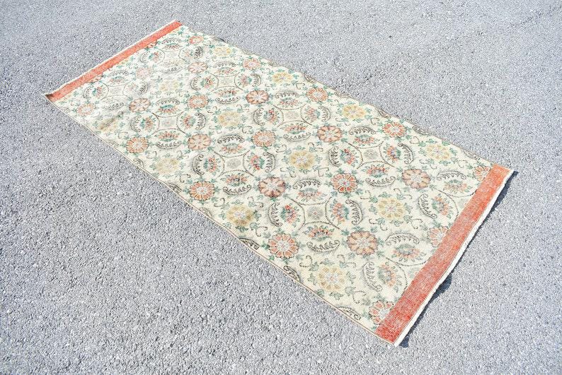 May include: Rectangular rug with a cream-colored background and a repeating floral pattern in shades of orange, green, and yellow. The rug has a faded, vintage look with an orange border.