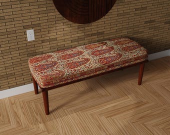 May include: A rectangular bench with a patterned cushion featuring red, orange, and blue paisley designs on a cream background. The wooden frame and legs are a dark brown color. The bench is approximately 48 inches long.