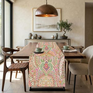 May include: A decorative table runner with a detailed floral and paisley pattern in shades of pink, green, and cream. The runner is placed on a wooden dining table, adding a touch of elegance to the dining room setting.
