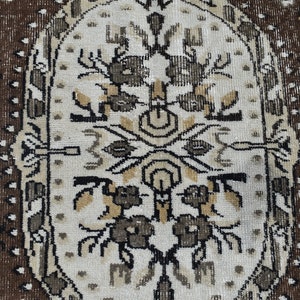 May include: A close-up of a beige rug with a brown border. The rug has a repeating pattern of stylized flowers and leaves in black, brown, and beige.