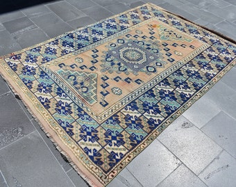 May include: A vintage rug with a beige background and intricate blue, green, and gold geometric patterns. The rug has a fringed edge.