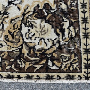 May include: Close-up of a brown and cream rug with a floral pattern. The rug has a fringe border and is made of a woven material.