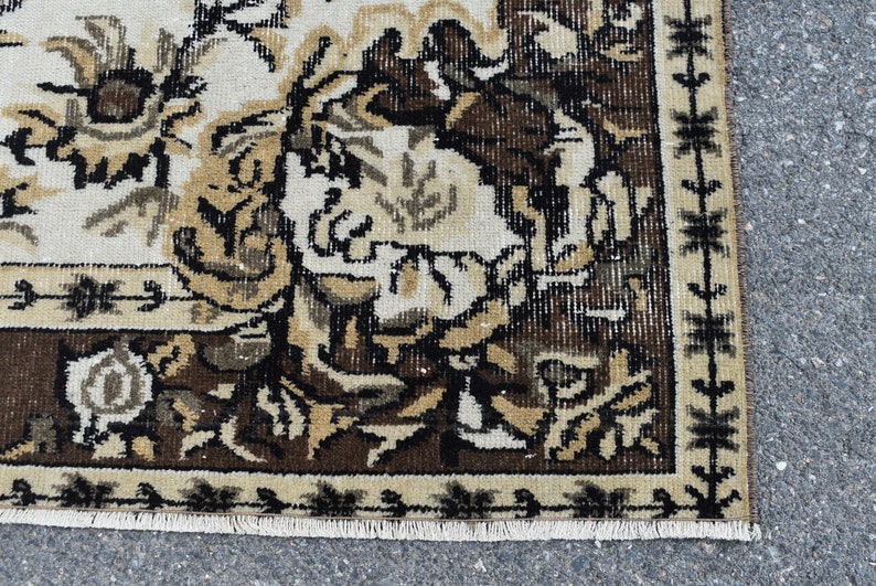 May include: Close-up of a brown and cream rug with a floral pattern. The rug has a fringe border and is made of a woven material.