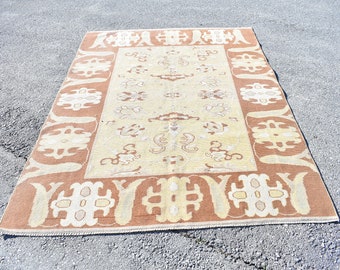 May include: A vintage rug with a beige background and a brown border. The rug has a traditional design with intricate patterns and floral motifs.