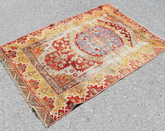 May include: A vintage Turkish rug with a red, yellow, and blue geometric pattern. The rug has a central medallion and a border with intricate details.