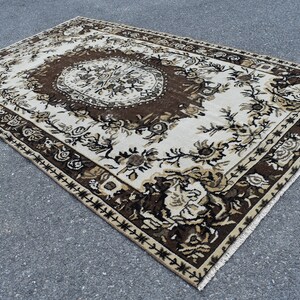 May include: A vintage rug with a floral pattern in shades of brown, beige, and white. The rug has a central medallion and a border with a geometric design.