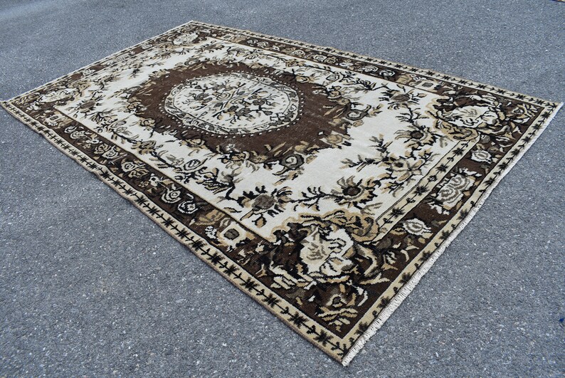 May include: A vintage rug with a floral pattern in shades of brown, beige, and white. The rug has a central medallion and a border with a geometric design.