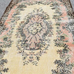 May include: An antique-style rug with a central floral medallion in peach and cream, surrounded by a border of dark brown and floral patterns. The rug has a distressed look, with faded colors and a vintage aesthetic.