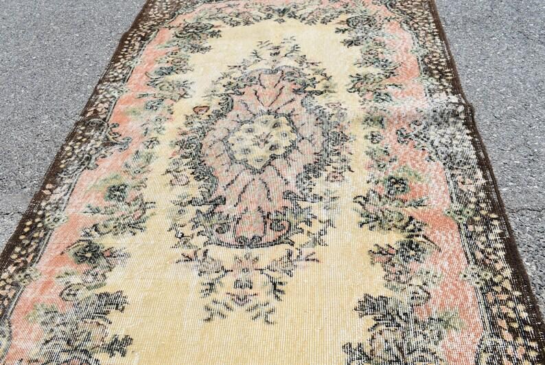 May include: An antique-style rug with a central floral medallion in peach and cream, surrounded by a border of dark brown and floral patterns. The rug has a distressed look, with faded colors and a vintage aesthetic.