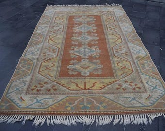 May include: Rectangular area rug with a central orange field and a patterned border. The rug features floral and geometric designs in shades of beige, yellow, and blue. White fringe trims the edges.
