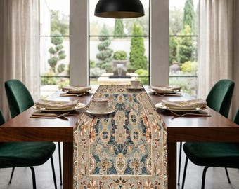May include: A rectangular table runner with an intricate floral pattern in shades of blue, beige, and rust. The runner is placed on a dark wooden dining table set with plates, cups, and silverware. The room has large windows and green velvet chairs.
