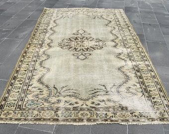 May include: A vintage rug with a light green background and a beige and brown floral pattern. The rug has a fringed edge.
