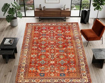 May include: A large, rectangular red rug with an intricate floral pattern. The rug features a central field of red with blue, beige, and gold accents. A detailed border frames the design, adding to its traditional aesthetic. The rug is placed on a hardwood floor.