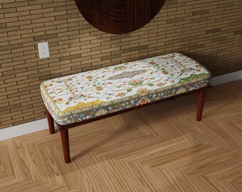 May include: A decorative bench with a rectangular seat featuring a colorful floral pattern on a white background. The bench has a dark brown wooden frame and legs. The seat is approximately 48 inches long.