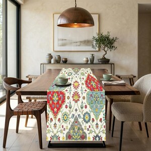 May include: A colorful table runner with a traditional floral pattern in red, blue, yellow, and green. The runner is placed on a wooden dining table, adding a decorative touch to the dining room. The runner's design features intricate details.