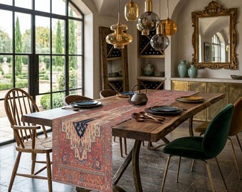 May include: A dining room table set for a meal, featuring a long, wooden table with a patterned runner. The runner has a red, blue, and cream design. Overhead, several pendant lights hang, and a large window offers a view of a garden.